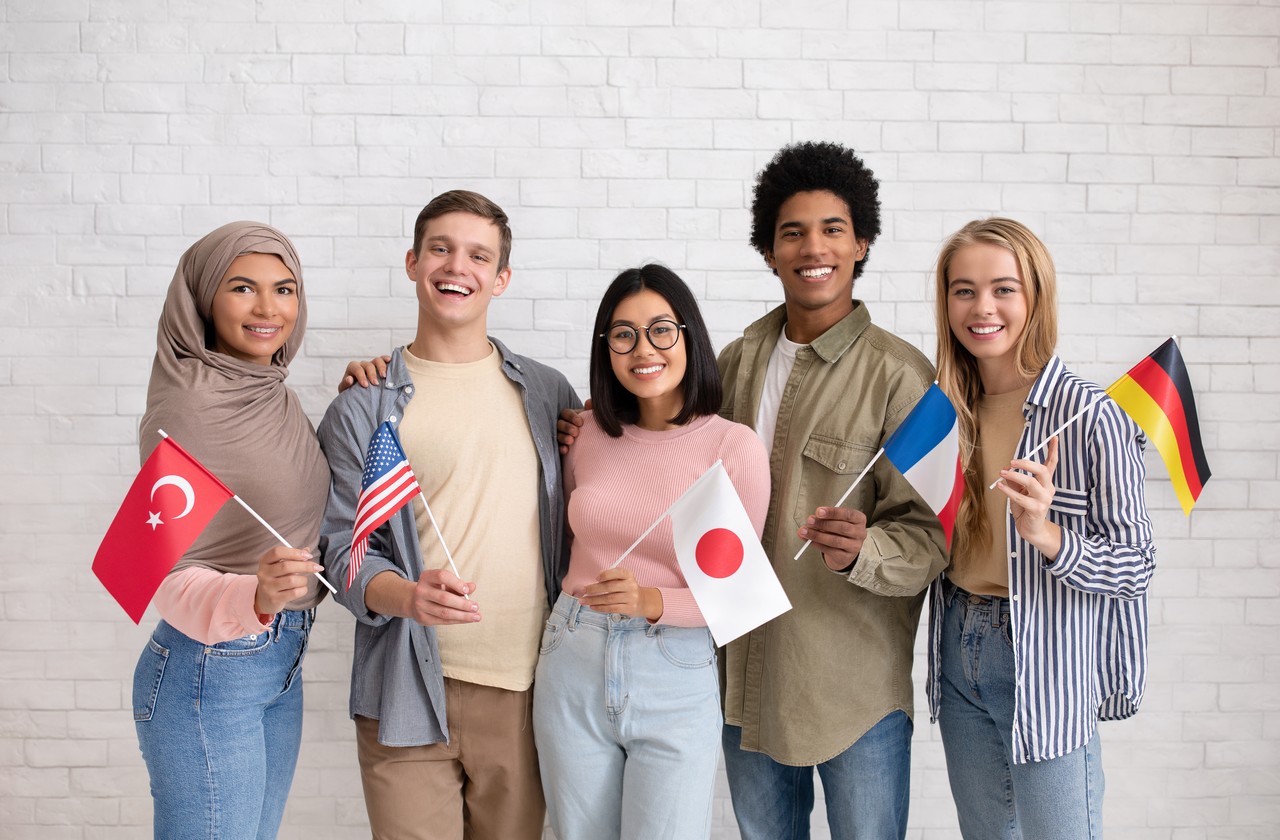 Student exchange, international friendship. Multiethnic young students with flags of different countries ready to study and look at camera on brick white wall background, studio shot, free space